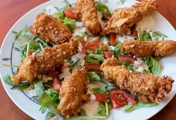 Chicken Strips na rucoli kawałki piersi kurczaka panierowane w specjalnej panierce, frytowane, podane na rucoli z plasterkami pomidora i polanej sosem czosnkowym