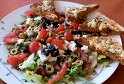 Hermosa Manana sałata lodowa z rucolą, plasterkami pomidora, pomidorem suszonym, oliwkami, serem feta, prażonymi pestkami z dyni i słonecznika oraz grzaneczkami z opiekanej tortilli